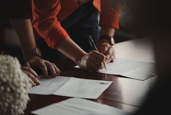 Image: view of arms and hands of two people signing documents.