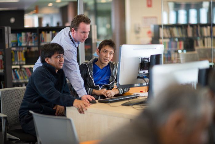 Image: A staff member assisting people to use the computers in the library