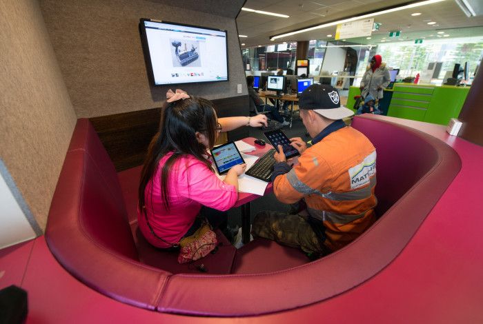 Image: a staff member helping a person use a device in the library.