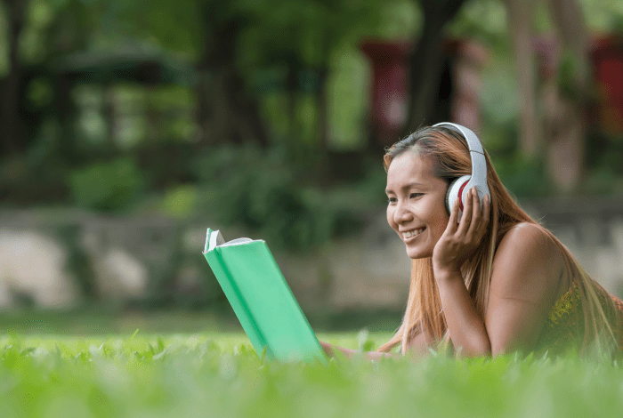 Image: A woman lying on the grass wearing headphones looking at a laptop computer