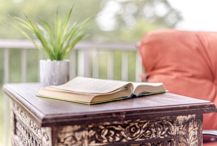 Image:  a book on a table next to a chair outside near a garden