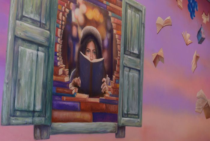 Image: Mural painting of a child sitting by window reading a book.