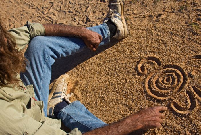 Indigenous man sitting on the ground drawing symbols.