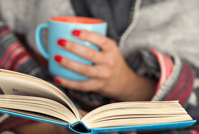 A person holding a drink mug and reading.