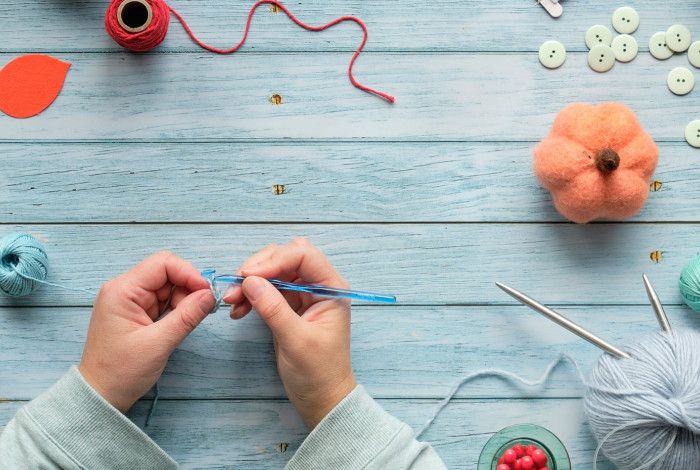 Hands crocheting over desk covered in yarn.