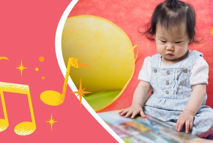 A baby looking at a picture book. There are toys and brightly coloured musical notes.