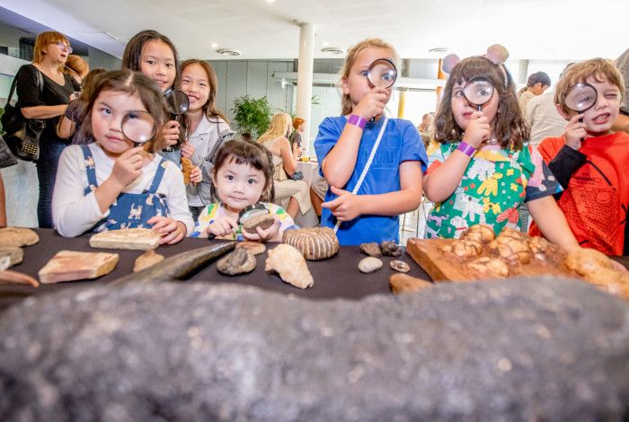 Children using magnifying glasses to explore fossils at a dinosaur discovery event.