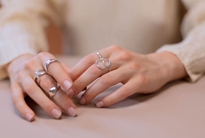 A pair of hands wearing five silver rings.
