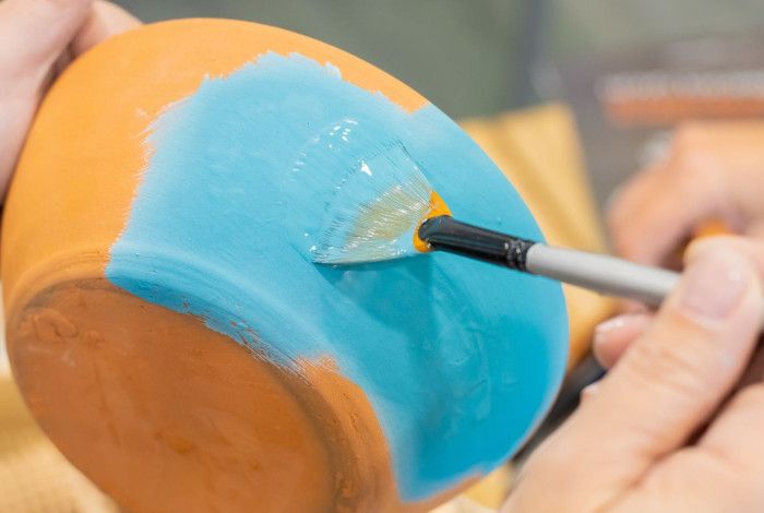 Close up of person's hands painting a terracotta pot.