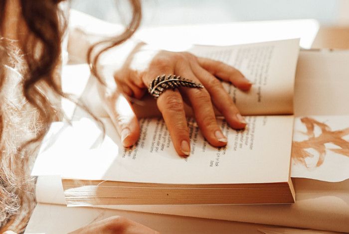 Person reading in a sunlit room, with a hand on the pages.