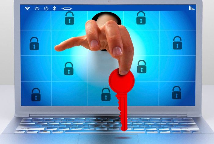 A hand reaching out of a laptop screen, holding a red key. 