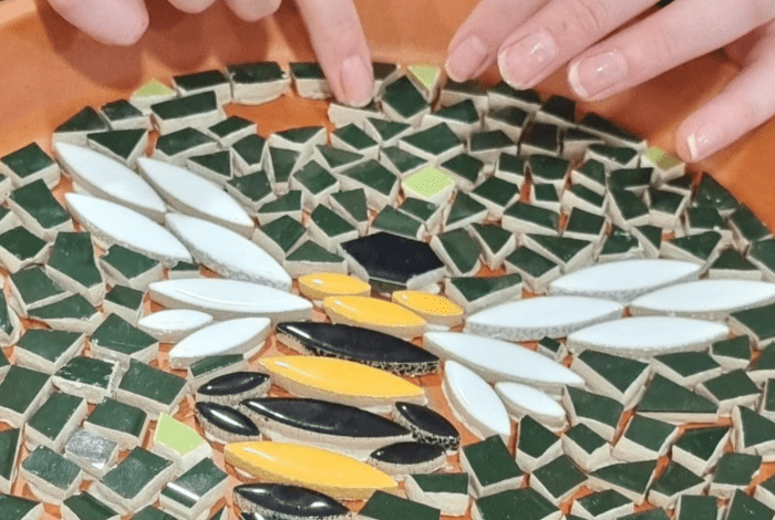 Hands handling and organising mosaic pieces to create a bee shaped image.