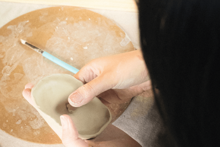 A person holding a piece of clay, creating a vessel shaped object.