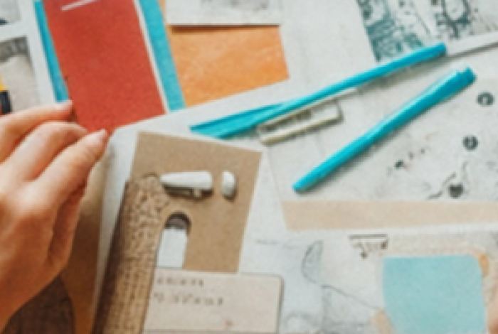 A person drawing with various notebooks and images scattered around