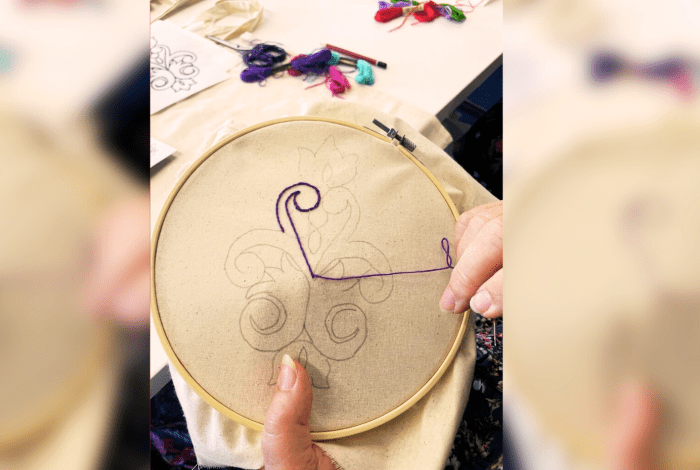A woman working on her embroidery using equipment including hoop, canvas, patterns and colourful threads.