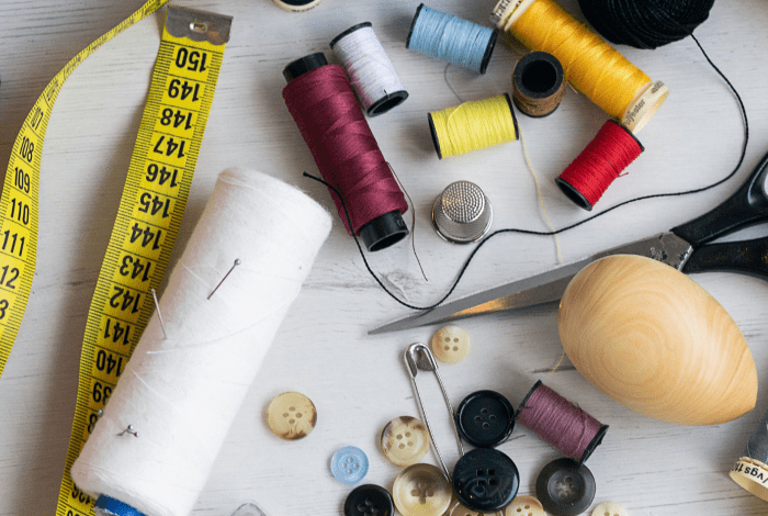 Sewing items on a table, including measuring tape, scissors, thread, pin and buttons.