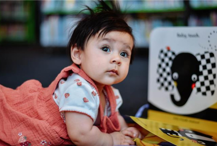 An infant on the floor with a board book.
