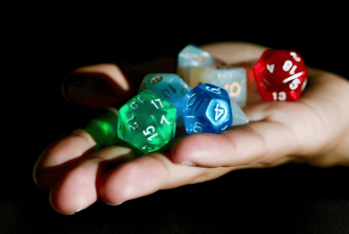 A hand holds several colorful multi‑sided tabletop gaming dice against a dark background.