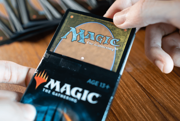 A close up image of hand opening a Magic the Gathering booster pack on a wooden table. 
