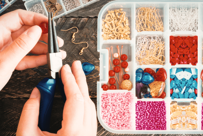 Someone using pliers to create bead and wire jewellery next to a sorted bead container. 