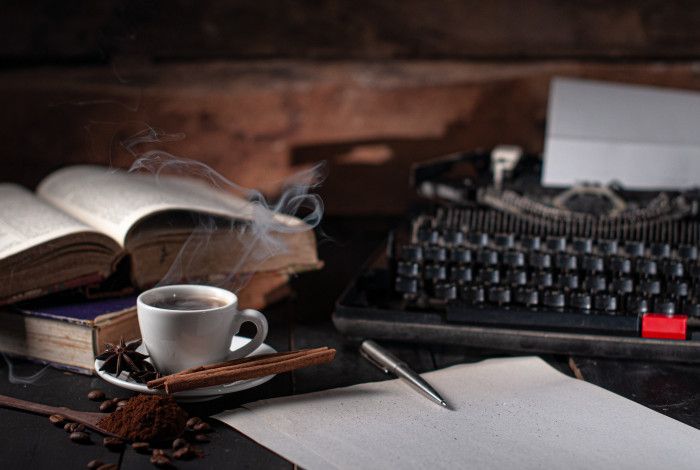 Books, tea and spices laid out on a table with pen, paper and a typewriter.