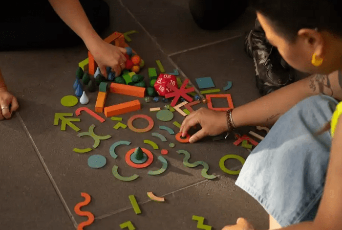 People collaboratively explore colourful geometric shapes and building pieces spread across a floor.