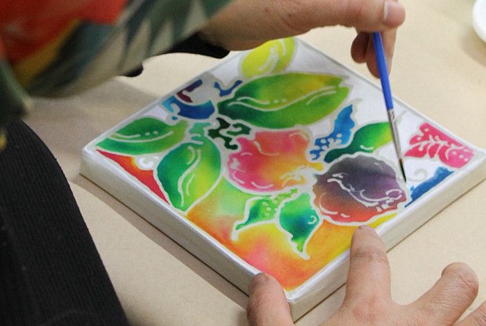 A person holding a paintbrush and painting a colourful image on batik.
