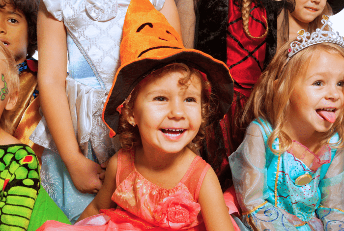 Children dressed in colourful Halloween and fairy tale costumes smiling together at a toddler event.
