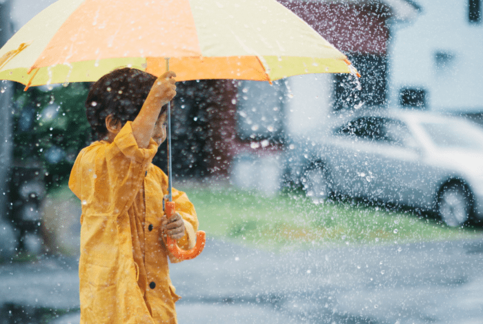 A child in a yellow raincoat holding an umbrella in the rain.