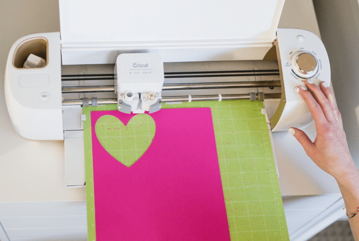 A person creating love heart shapes out of a pink coloured material on a Cricut machine.
