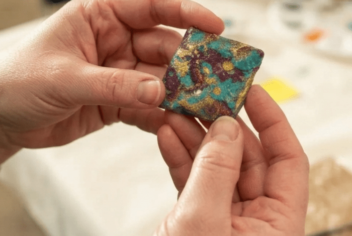 Hands holding a colourful, painted, square stone. 