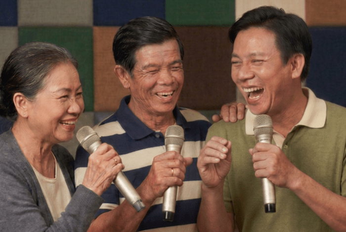 Three older people, a woman and two men, singing karaoke together and having fun.