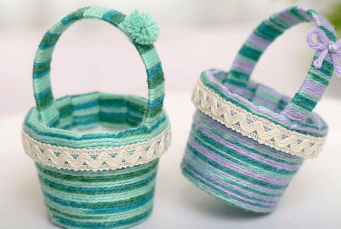 Two small woven baskets wrapped in green, blue and purple yarn with decorative trim and handles.
