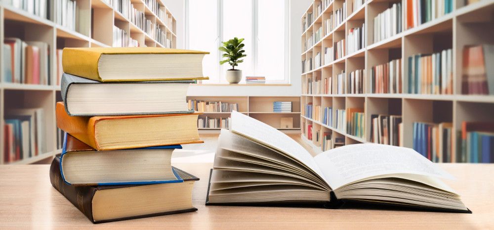 Table with an opened book and stack of five books beside it.