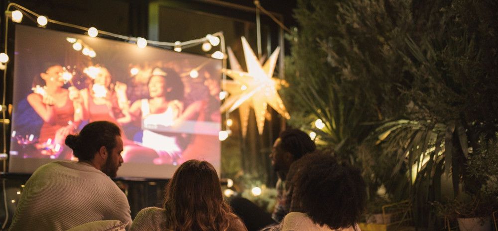 Group of people watching a movie on a screen outdoors.