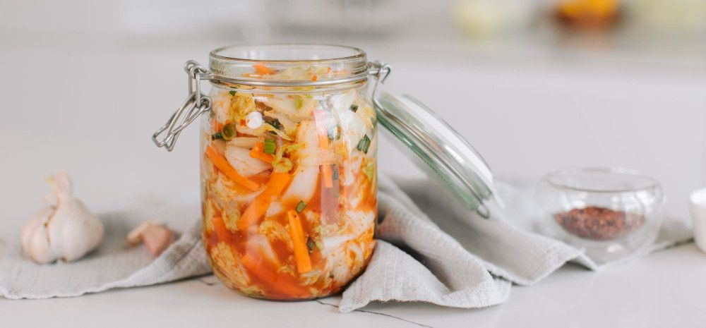 Jar of Kimchi open next to a garlic bulb.