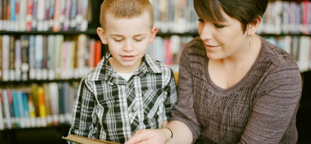 Parent reading with child in a library.