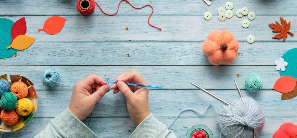 Hands crocheting over desk covered in yarn.