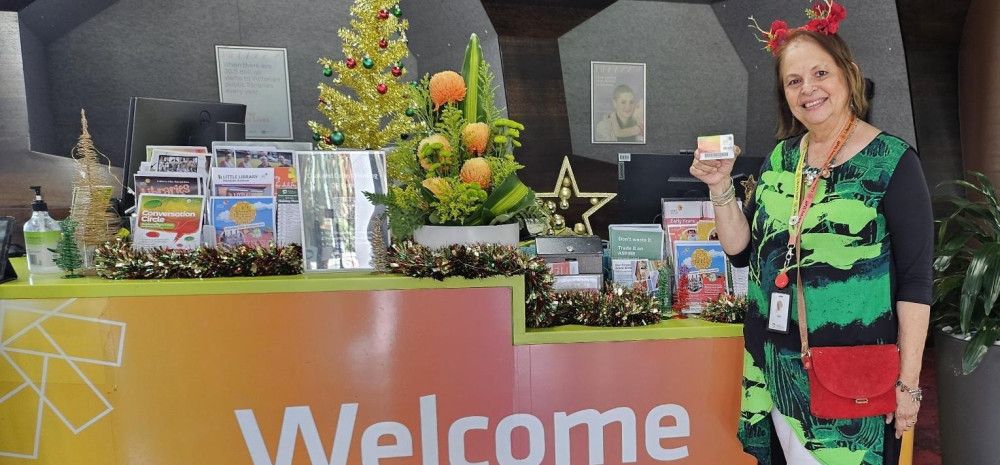 Staff member at the Dandenong Library service desk holding a membership card.