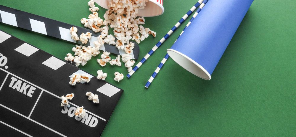 Clapperboard, popcorn and drink cup on green background.