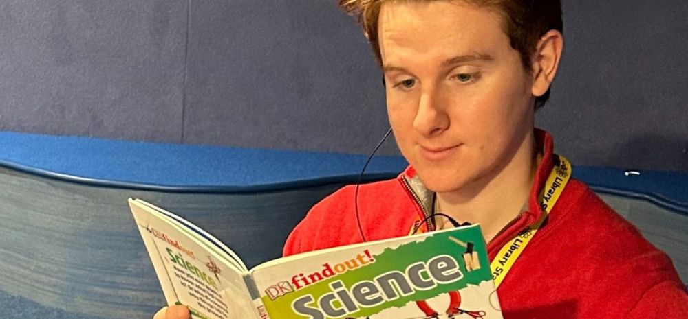 Young library staff member reading a book in the library.