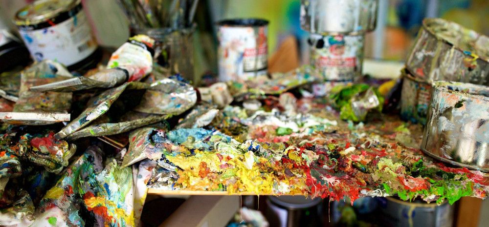 Empty paint tubes and cans covered in dried paint on a table.