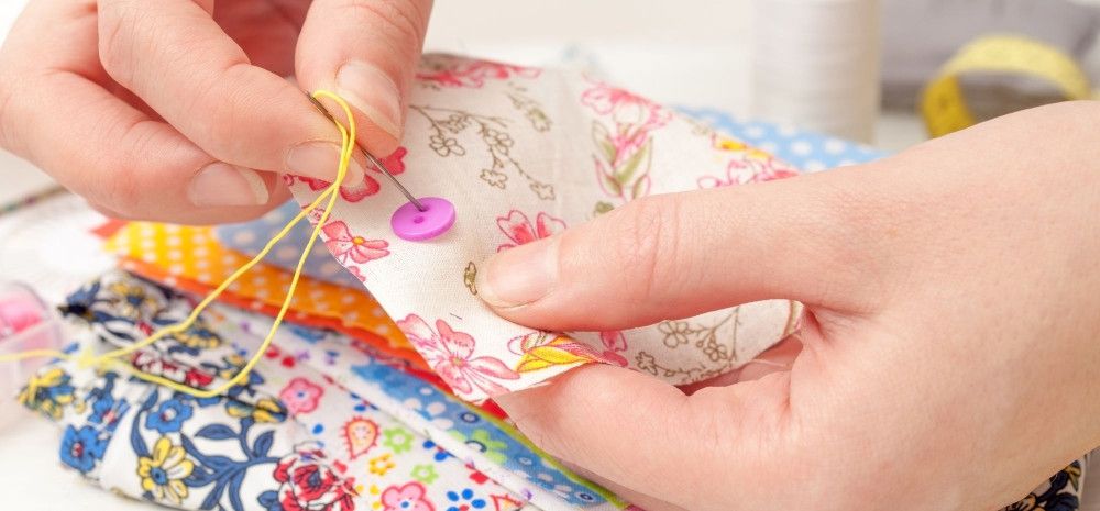Person sewing button to floral fabric square.