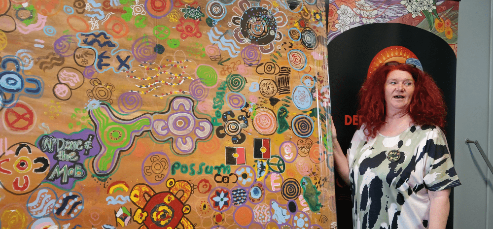 Arist N'Dene Riley standing beside an artwork.