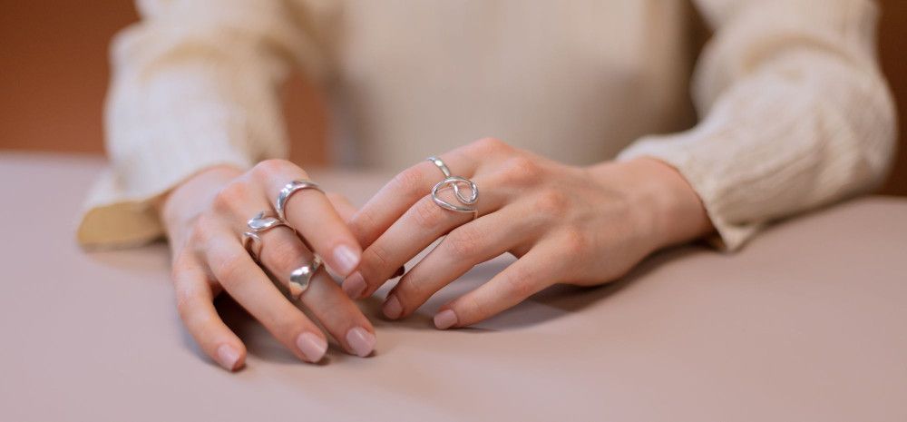 A pair of hands wearing five silver rings.