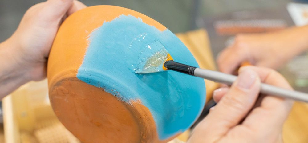 Close up of person's hands painting a terracotta pot.