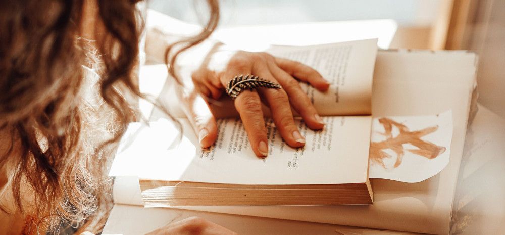 Person reading in a sunlit room, with a hand on the pages.