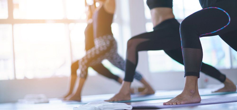 People in a yoga class holding a lunge pose on mats in a sunlit studio.