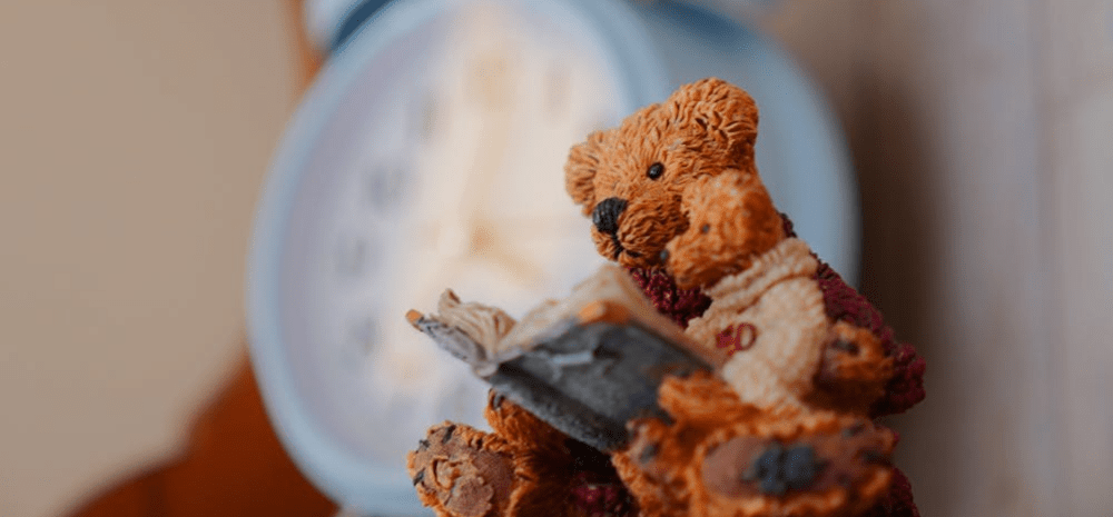 An ornament depicting a teddy bear holding a small teddy and reading a book together.