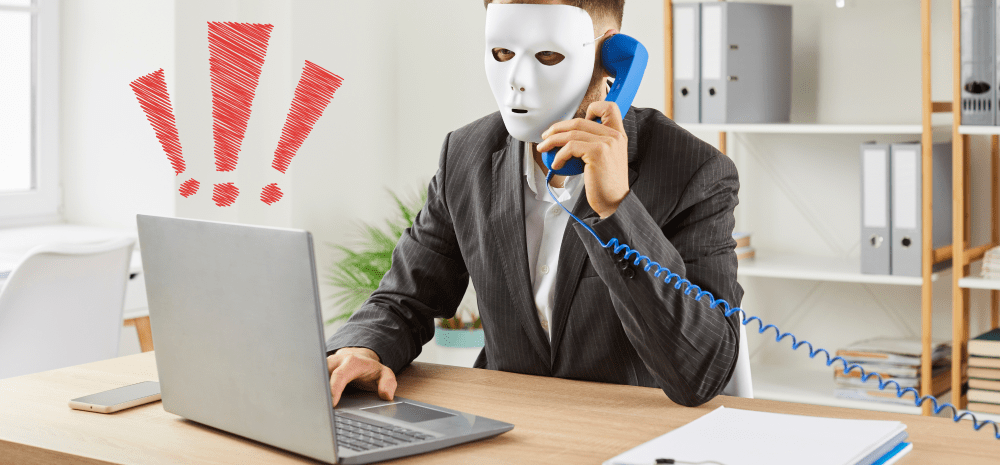 Suspicious looking man in a mask sitting at a laptop on a phonecall.